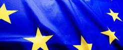 Flaga Unii Europejskiej z żółtymi gwiazdami na niebieskim tle. Flaga jest pofałdowana.