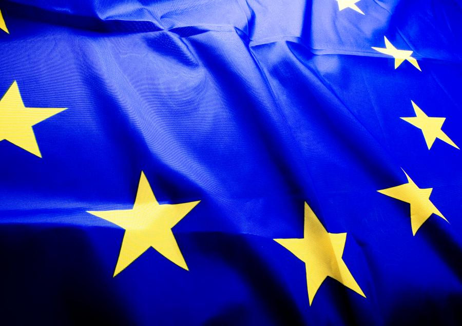 Flaga Unii Europejskiej z żółtymi gwiazdami na niebieskim tle. Flaga jest pofałdowana.